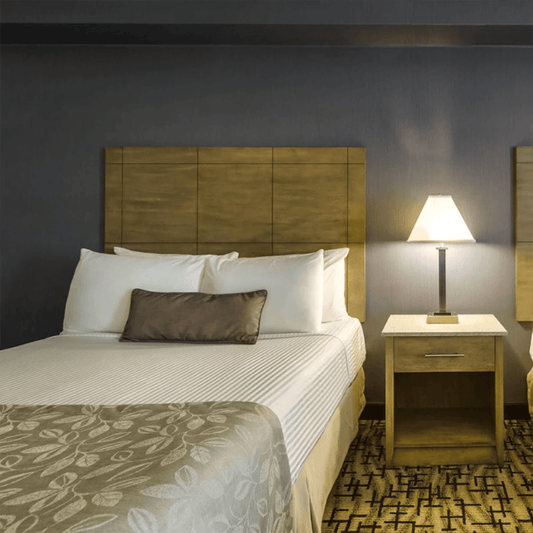 A hotel room with two beds that have white sheets. Towards the end of the beds there are beige bed scarf/ bed runner with off white designs facing a dresser with a TV. 